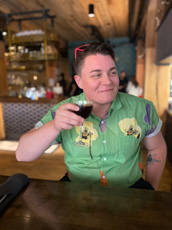 a man in a green shirt smiling to something off camera while holding a glass of wine